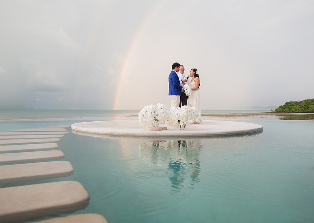 Couple exchanging wedding vows with rainbow overhead